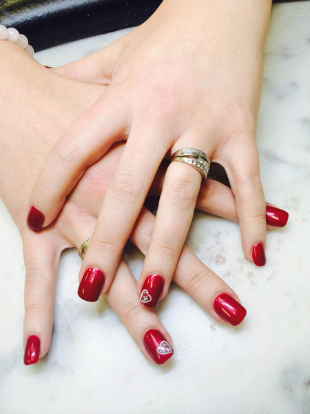 Squared gel nails in dark red with white heart flourishes on the ring fingers create a stunning display from Binh's on 17th.