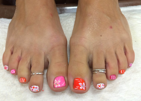 Decorated toenails in shades of pink and red with white accents designed by the nail techs at Binh's in Edmonton