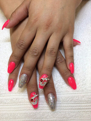 Feminine fingers with nails adorned with jewelled skulls, plain pink polish, and silver glitter is another Binh's Nails original