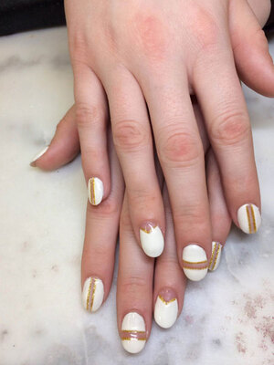 Stark white oval gel nails with a unique design in gold for every finger is a great style option from Binh's in East Edmonton.