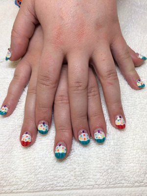 Young female hands with tiny blue cupcakes adorning the nails and contrasting red cupcakes on the ring fingers from Binh's Salon in Edmonton.