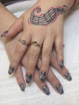 Tattooed female hands with oval gel nails in black, grey and glitter makes for a great look for younger clients.