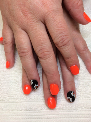 A woman's hands with orange polish on the nails and black polish with flowers on the ring fingers from Binh's