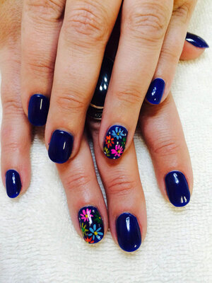 a pair of hands with shiny deep blue nails with fun floral features on the ring fingers from Binh's manicure artists
