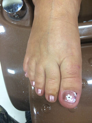 A female foot sporting clear toenail polish and a floral design on the big toe from Binh's; the place for eye-popping pedicures