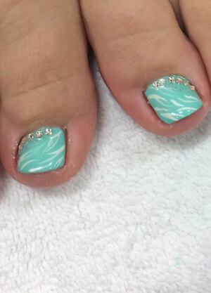 A pair of bare feet showing off turquoise toenails with glitter art accents from Binh's Nails pedicure pros.